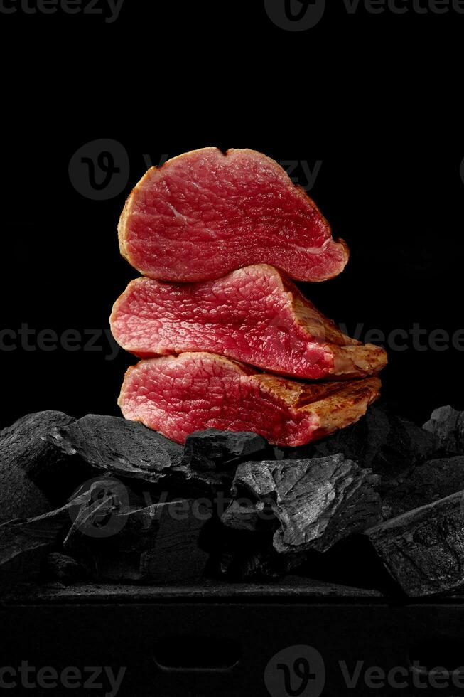 bitar av lätt stekt kalvkött fläskkarré på träkol på svart bakgrund foto