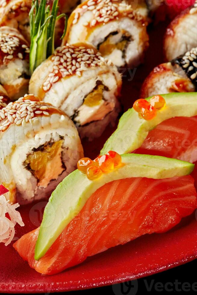 närbild av nigiri sushi med lax, avokado, röd kaviar och unagi rullar med ål, grädde ost och orange på röd tallrik foto