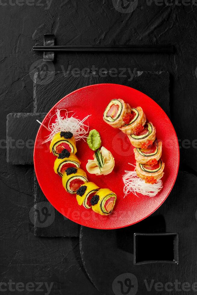 uramaki rulla med lax, tonfisk, mango, avokado, tobiko och röd kaviar på röd tallrik foto