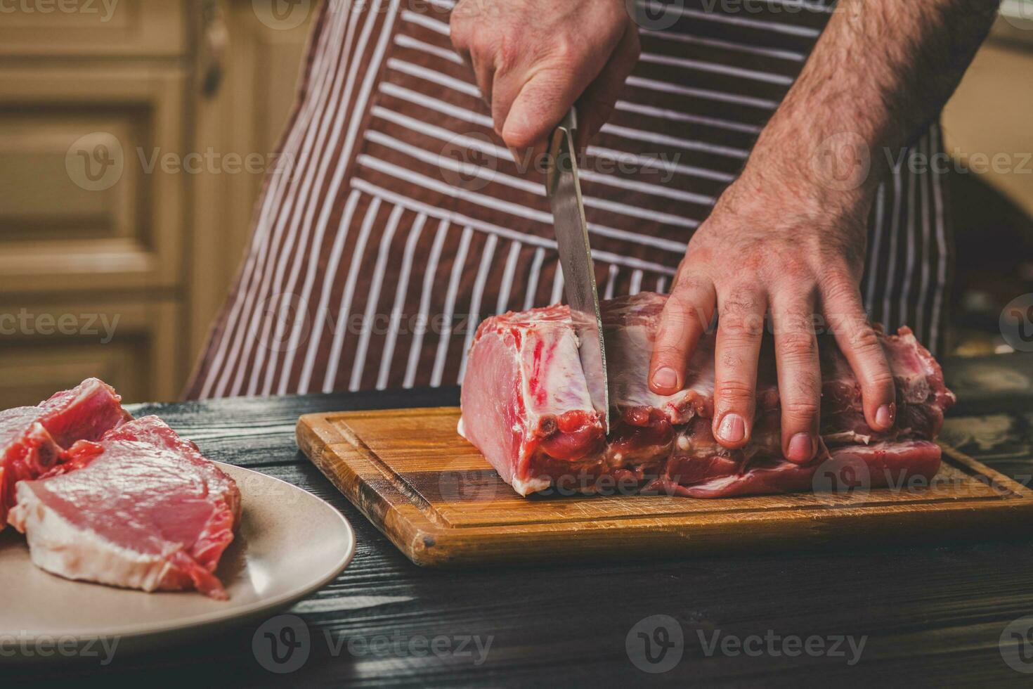 man nedskärningar av färsk bit av kött på en trä- skärande styrelse i de Hem kök foto