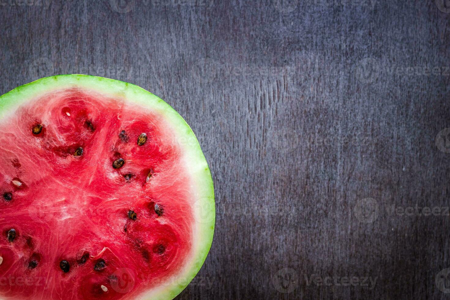 en halv av färsk vattenmelon på mörk trä- bakgrund. efterrätt. platt lägga, topp se foto