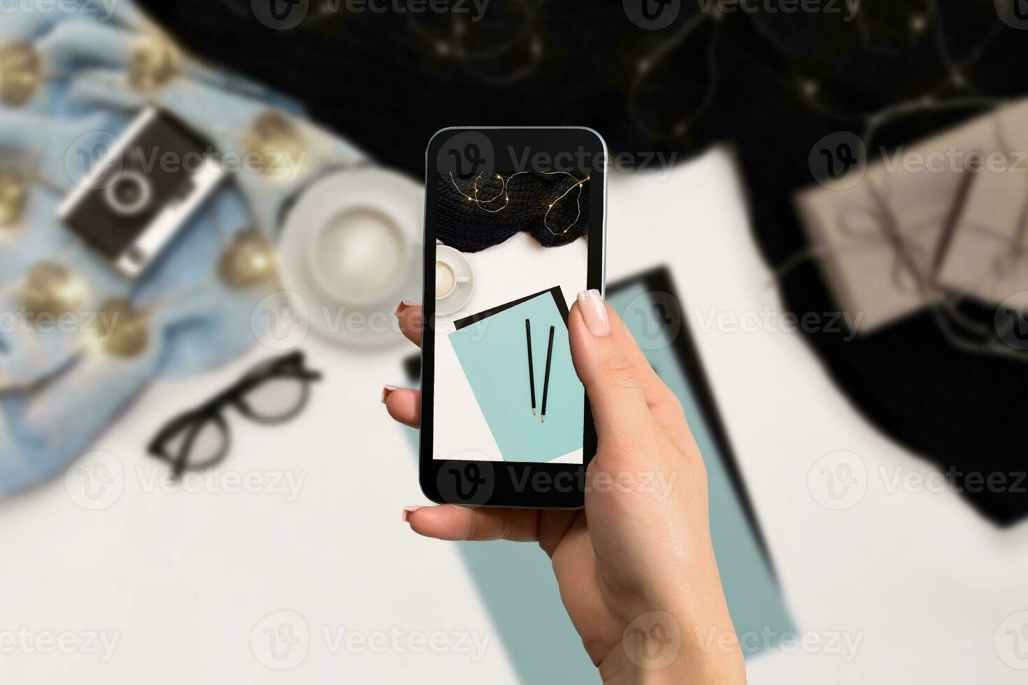 kvinna hand med en smartphone gör en Foto arbetsyta med anteckningsbok, kaffe kopp, scarf, glasögon.