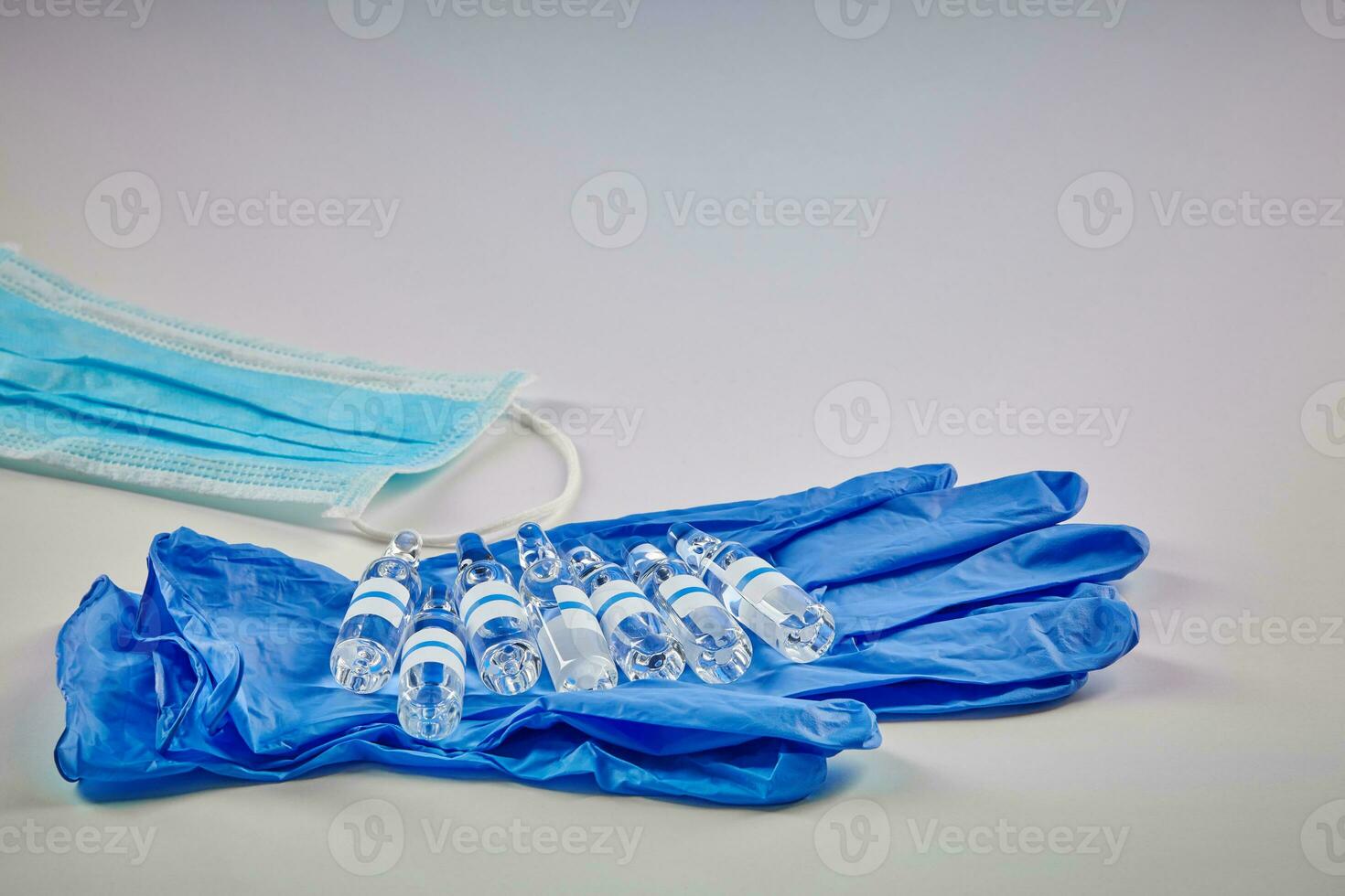 sju attrapp ampuller med transparent flytande på blå disponibel handskar och medicinsk mask isolerat på vit. coronavirus. pandemi covid19. stänga upp foto
