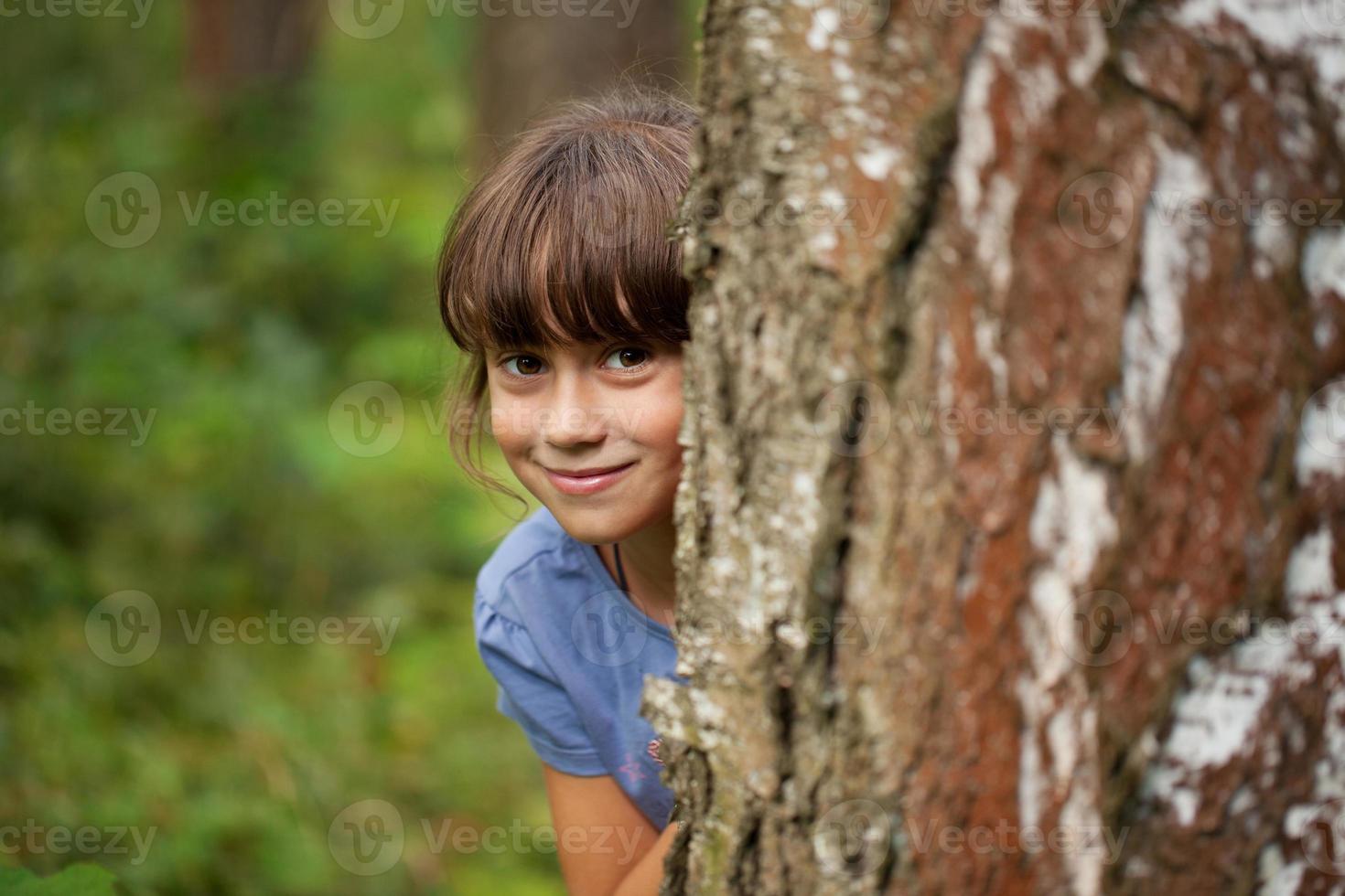liten flicka som kikar ut bakom en trädstam foto