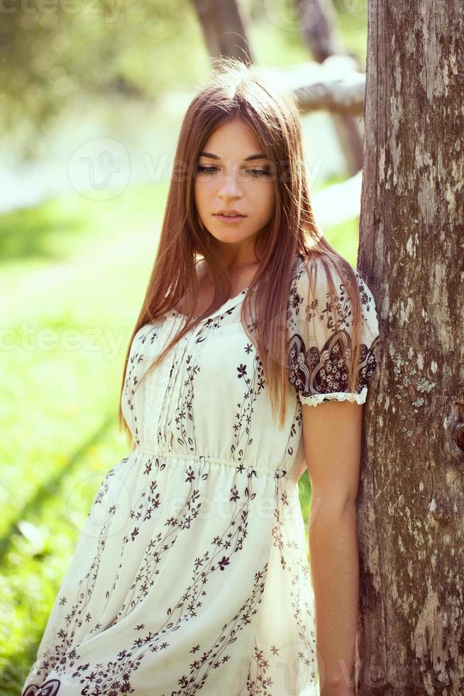 flicka i en sommarklänning lutad på ett gammalt träd foto