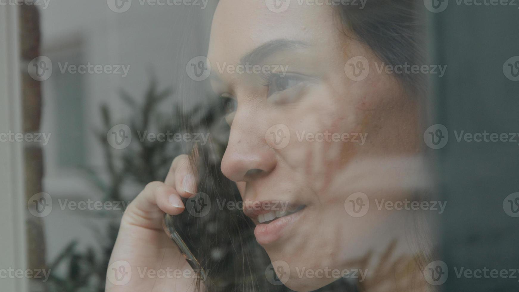 ung blandad ras kvinna som ringer medan hon tittar genom fönstret foto