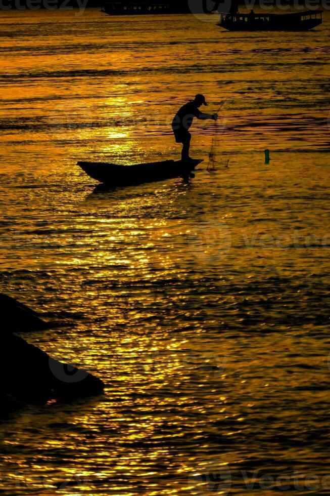 en man i en båt är fiske på solnedgång foto