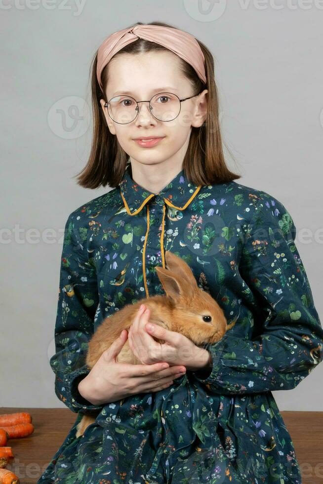 porträtt av en flicka i glasögon med en röd kanin. barn med en kanin. foto