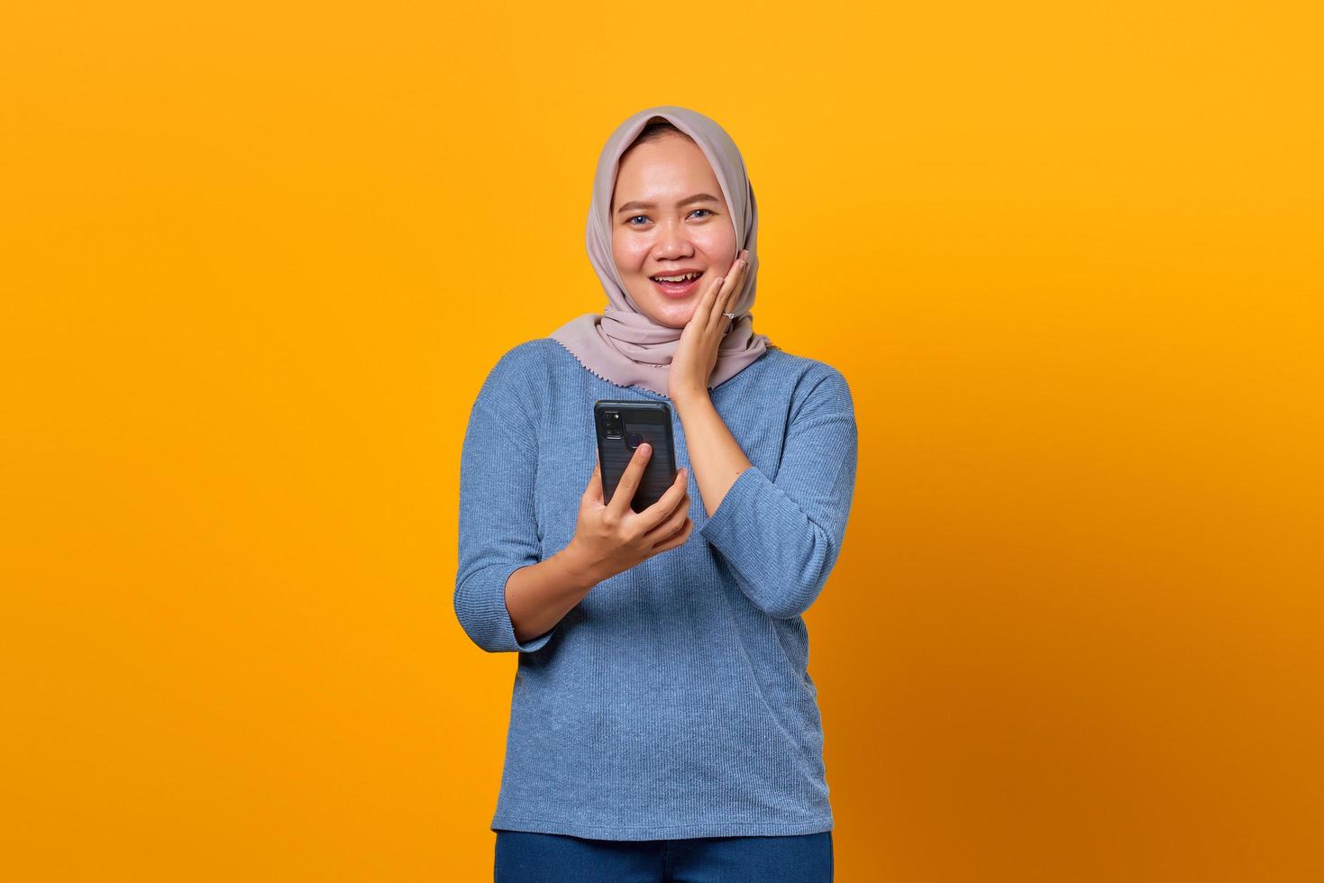 glad attraktiv asiatisk kvinna som använder mobiltelefon och rörande kinder foto