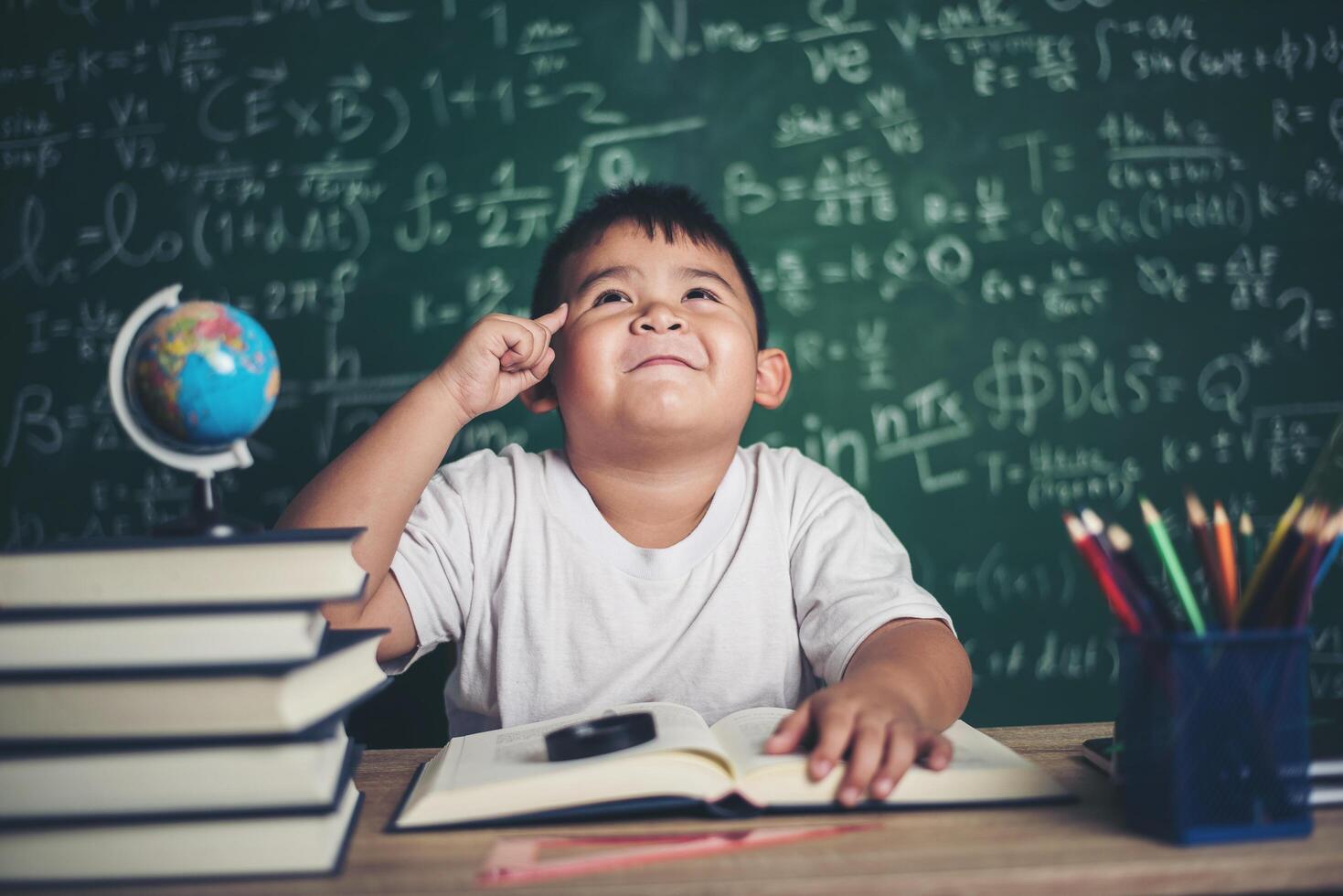 tankeväckande liten pojke med bok i klassrummet foto