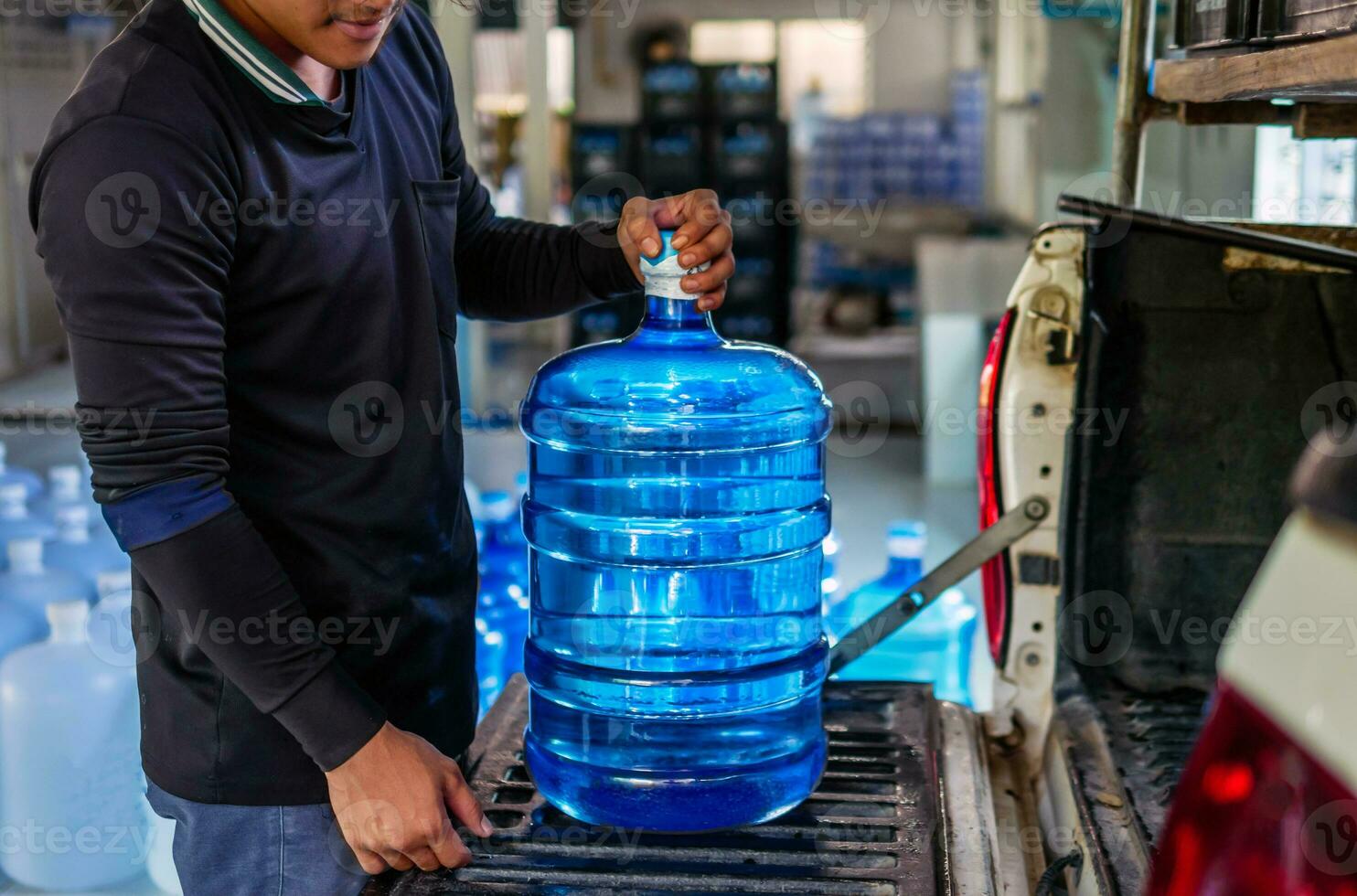 arbetare hiss dricka vatten klar och rena i blå plast gallon in i de tillbaka av en transport lastbil renades dricka vatten inuti de produktion linje till förbereda för rea.liten företag foto