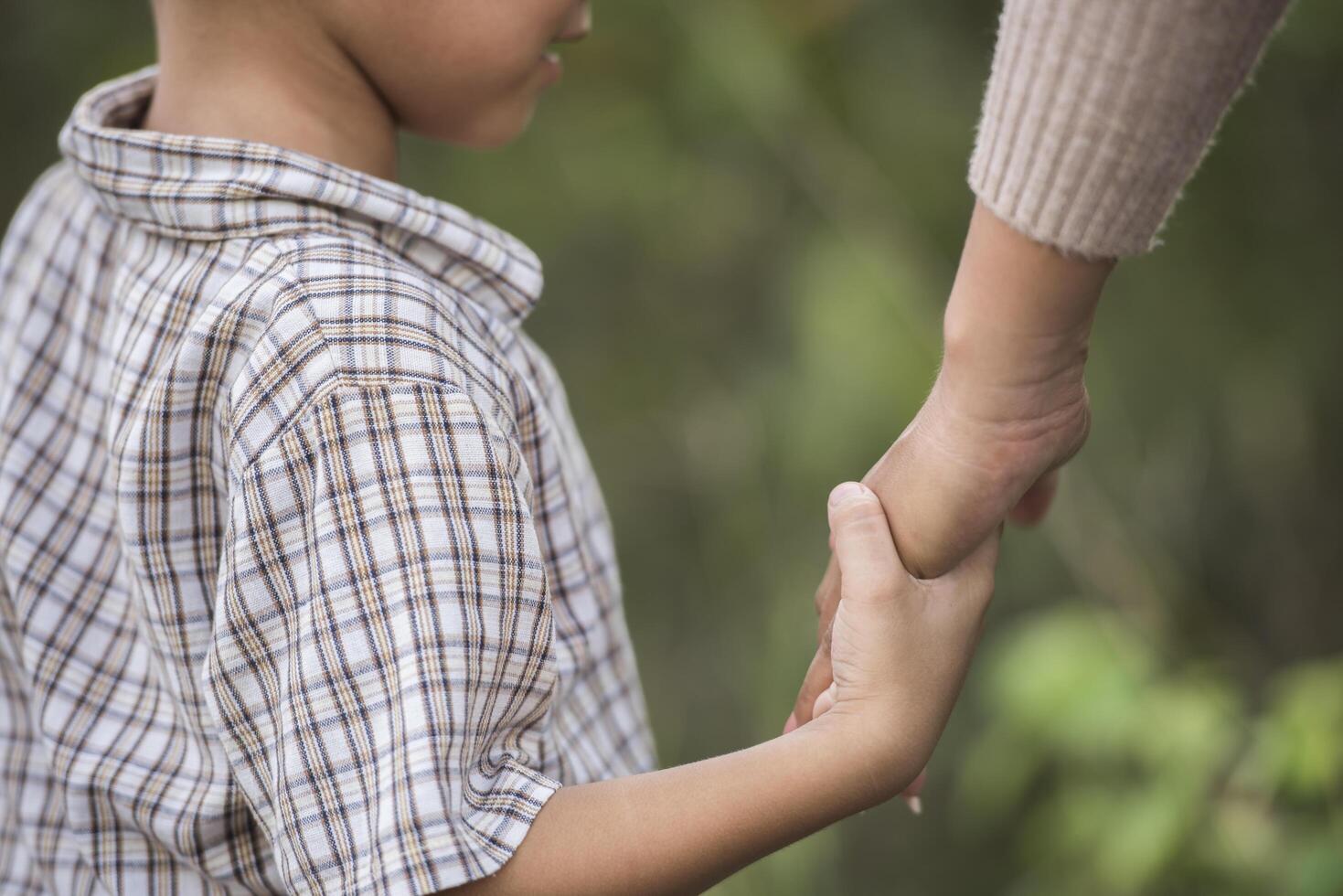 närbild av glad mamma och son som håller handen i en park. familjekoncept. foto