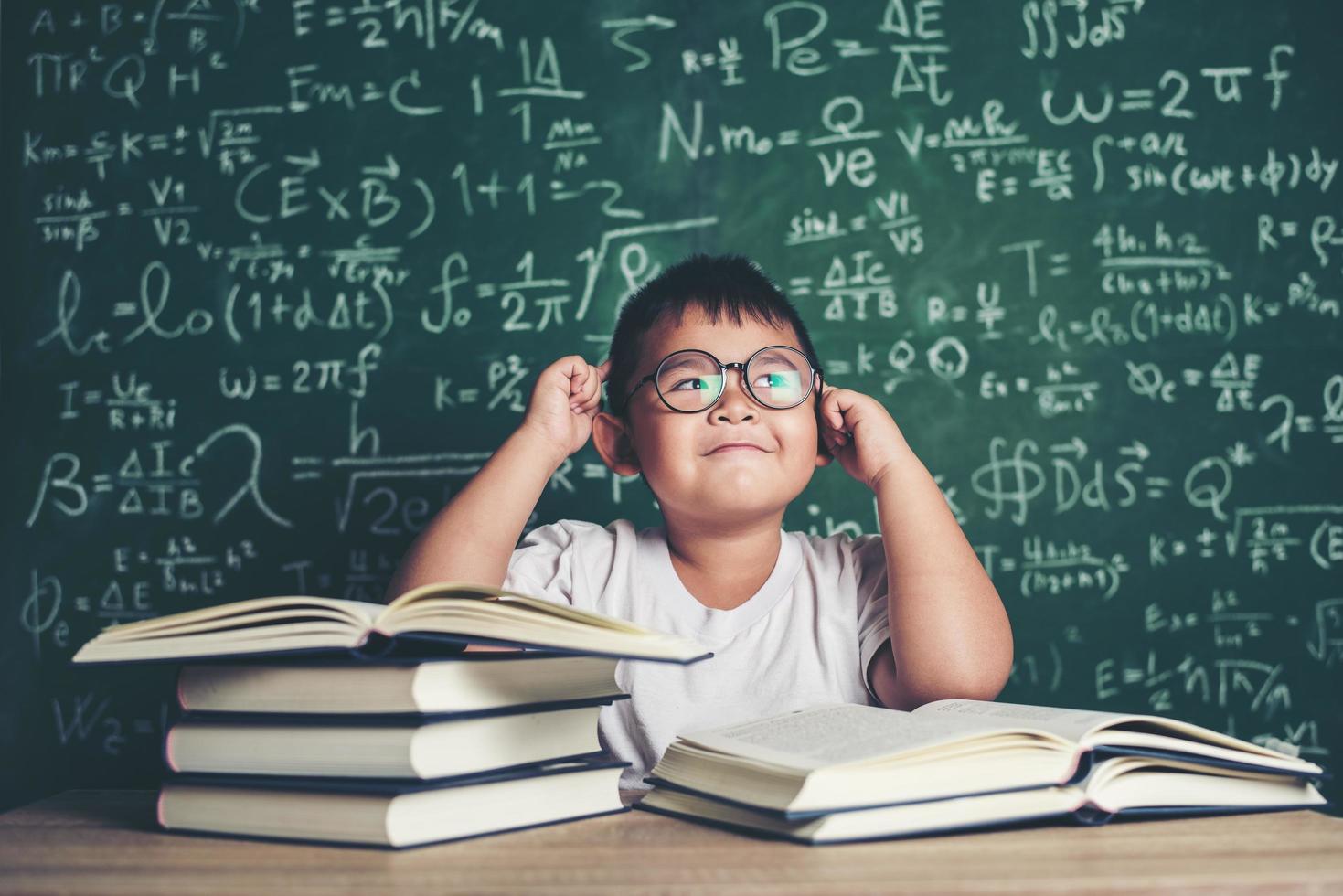 tankeväckande liten pojke med bok i klassrummet foto