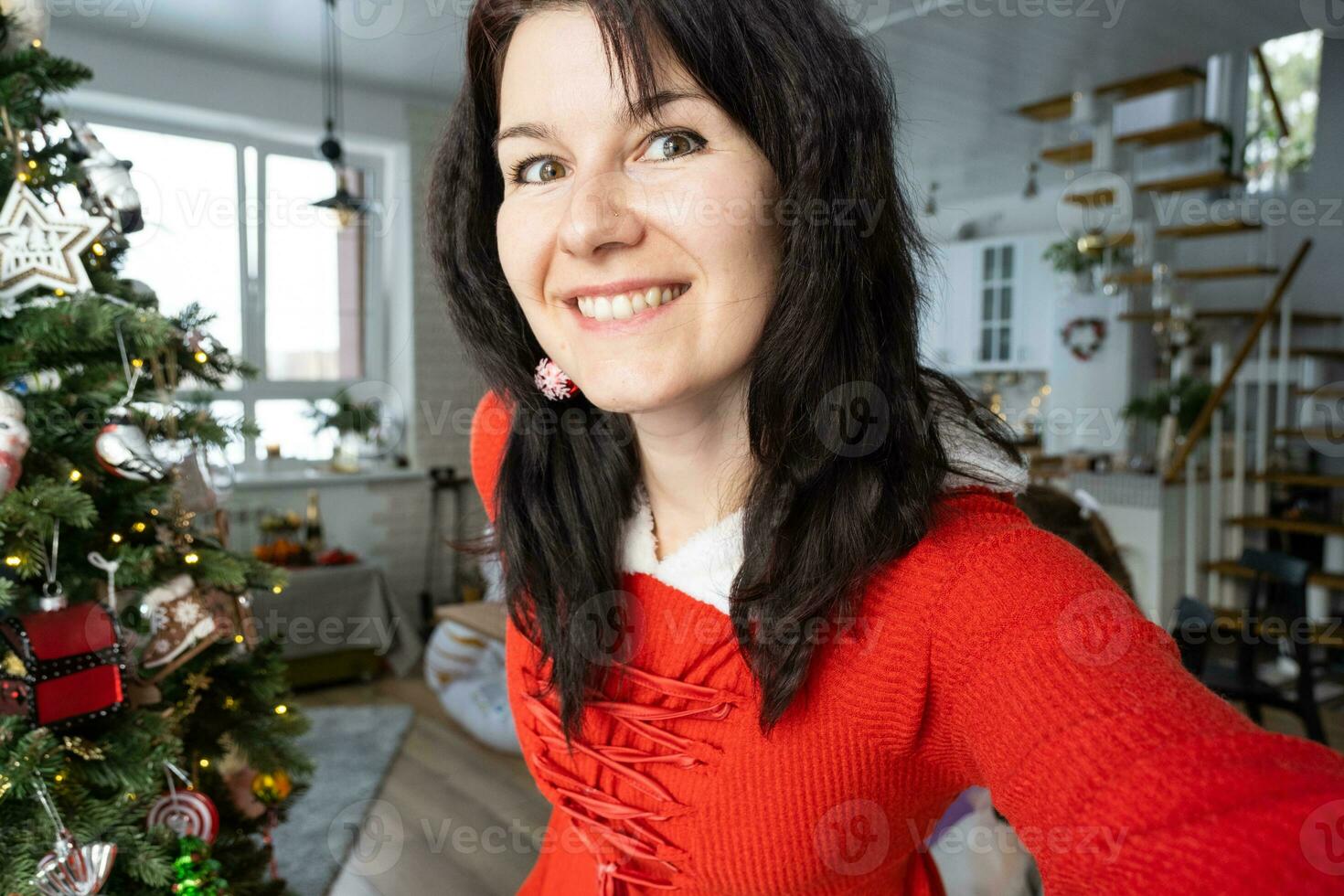 selfie porträtt av en kvinna i en röd santa klänning i en Hem interiör med en jul träd och ny år dekor. förberedelse för de högtider, fest foto