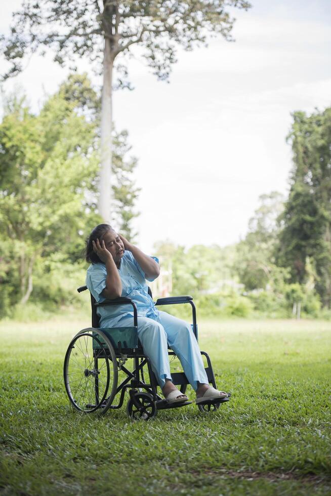 ensam äldre kvinna sitter ledsen på rullstolen i trädgården foto