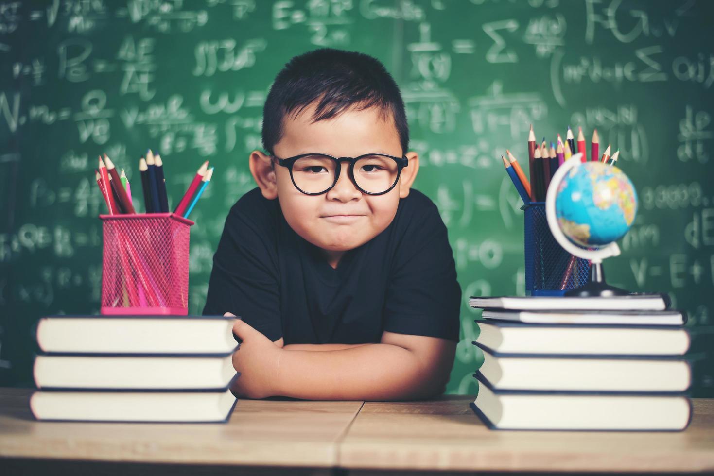 tankeväckande liten pojke med bok nära en skolbräda foto