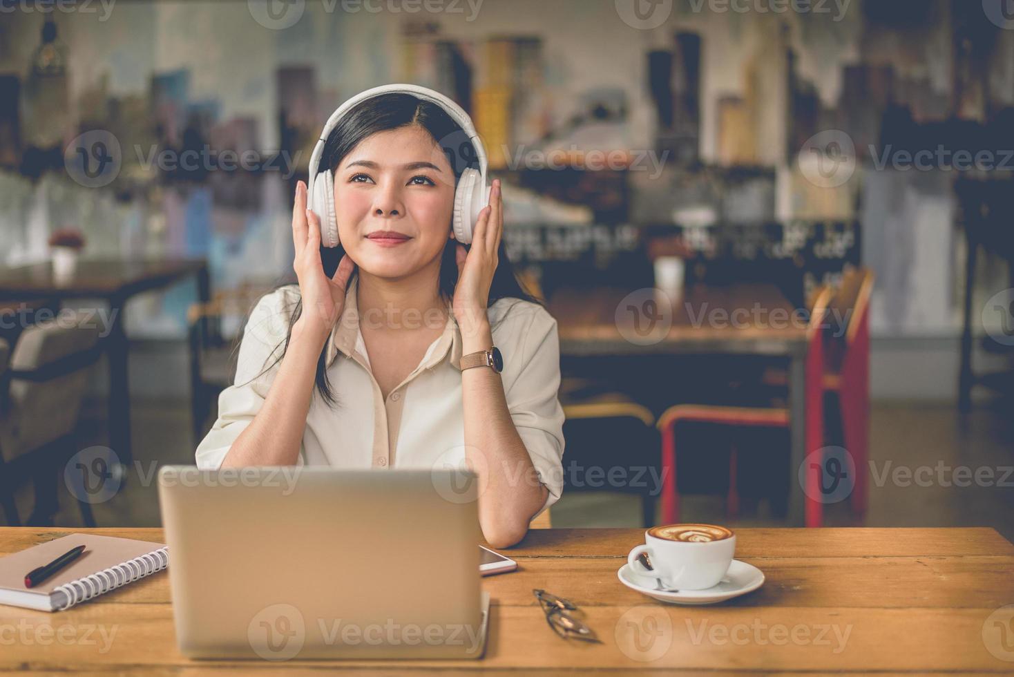 glad asiatisk kvinna som kopplar av och lyssnar på musik i kaféet foto