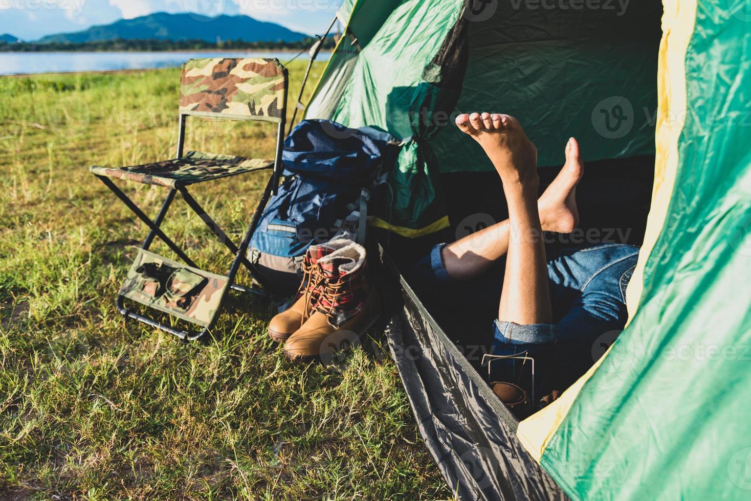 närbild av kvinnaben som kopplar av i campingtält med bergssjö foto