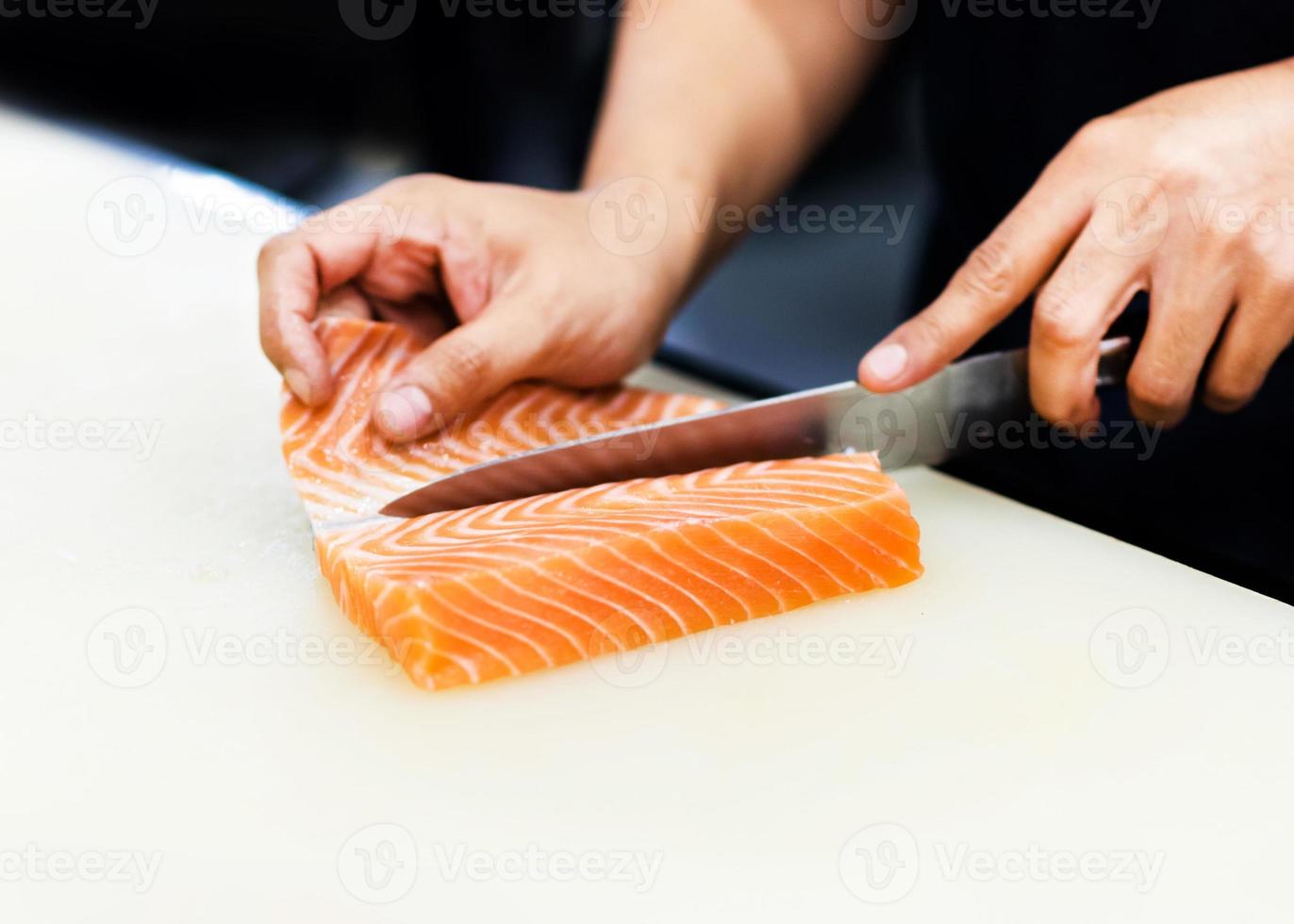 kock med en kniv för att skiva laxfilé i restaurangen foto