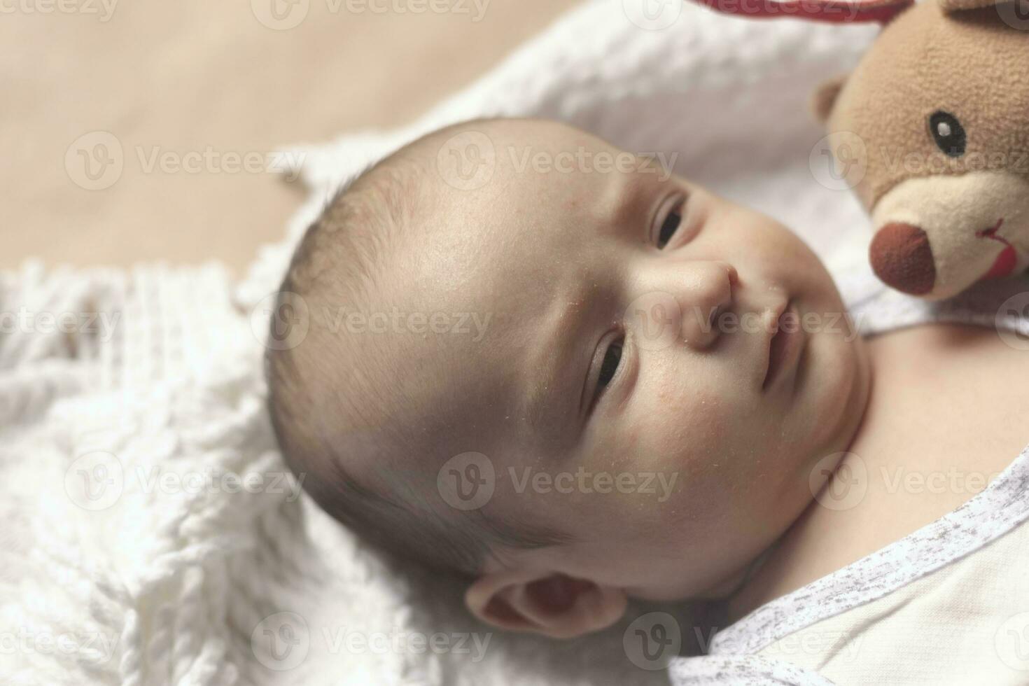 2 månad bebis pojke liggande. närbild av förtjusande söt nyfödd bebis pojke av två månader på mjuk textil. härlig barn spelar med plysch leksak foto