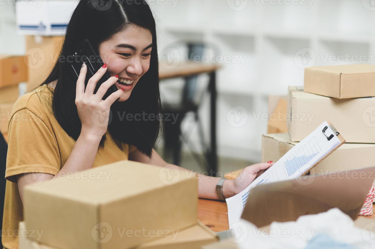 kvinna som säljer produkter online pratar i telefon och kontrollerar lager, foto