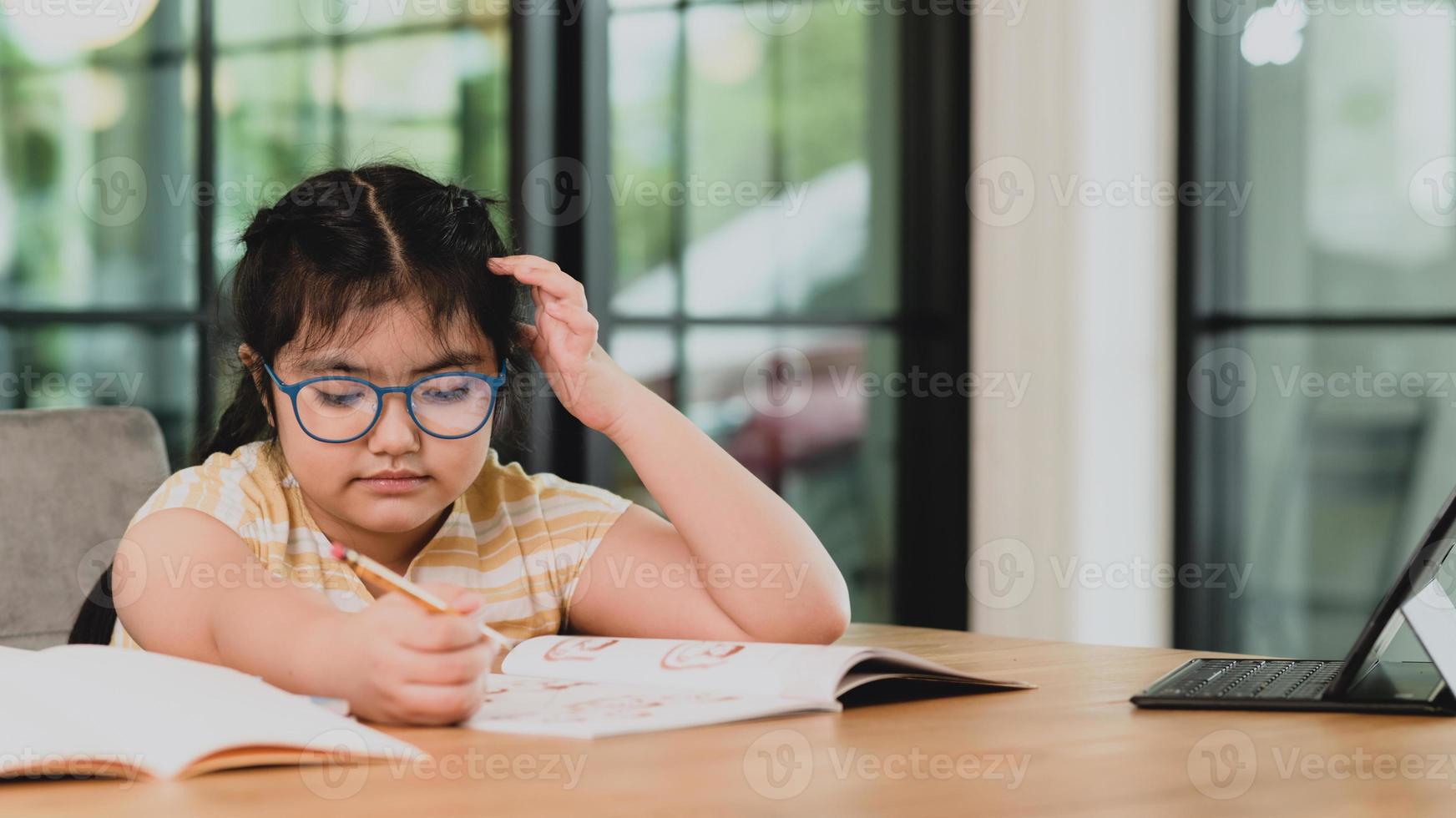 ett barn flicka i glasögon ritar i en anteckningsbok med en surfplatta. foto