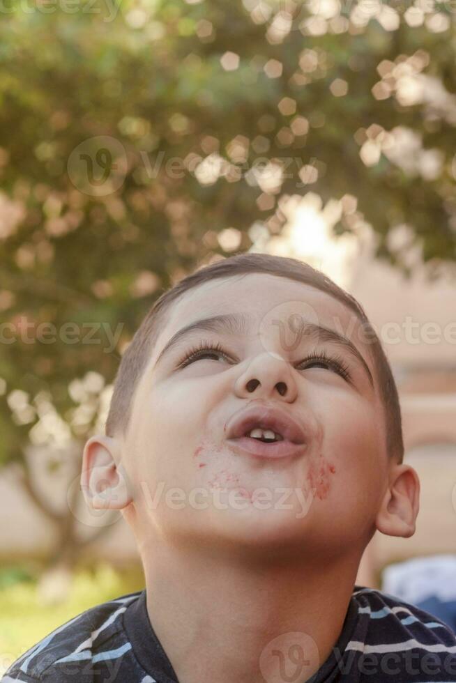 liten pojke vrider sig hans ansikte på utomhus. 6 år gammal unge i sommar högtider. söt liten pojke lurar runt om. människor, barndom livsstil begrepp. porträtt av ung barn framställning rolig ansikten foto