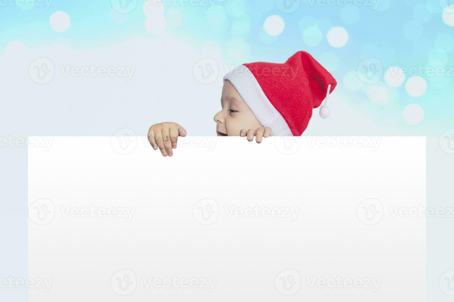 en liten pojke med santa keps innehav de tom papper. santa bebis pojke med ett tömma vit kort. kopia Plats för din reklam och text foto