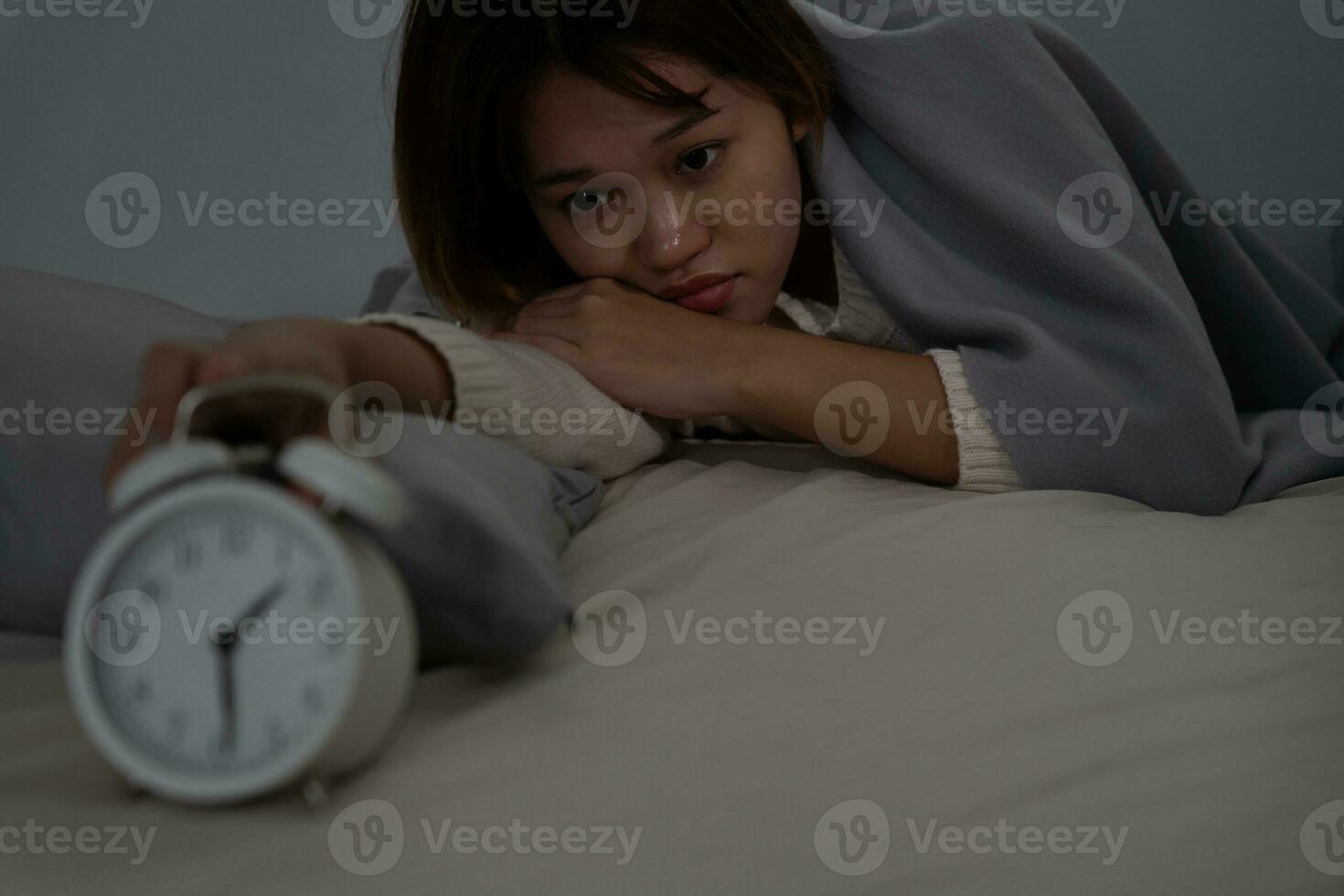 asiatisk kvinna i säng sent påfrestande till sömn lidande sömnlöshet, sömnlös eller rädd i en mardröm, ser ledsen orolig och stressad. trött och huvudvärk eller migrän vakna upp i de mitten av de natt. foto