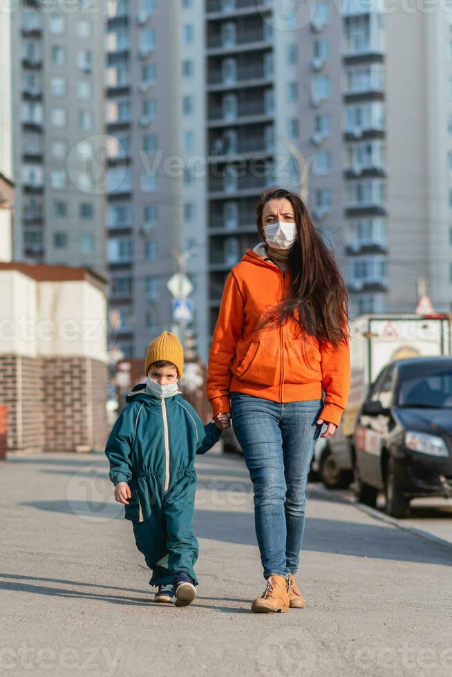 en mor med en bebis i medicinsk masker promenader ner de gata under de coronavirus pandemi och covid -19. foto