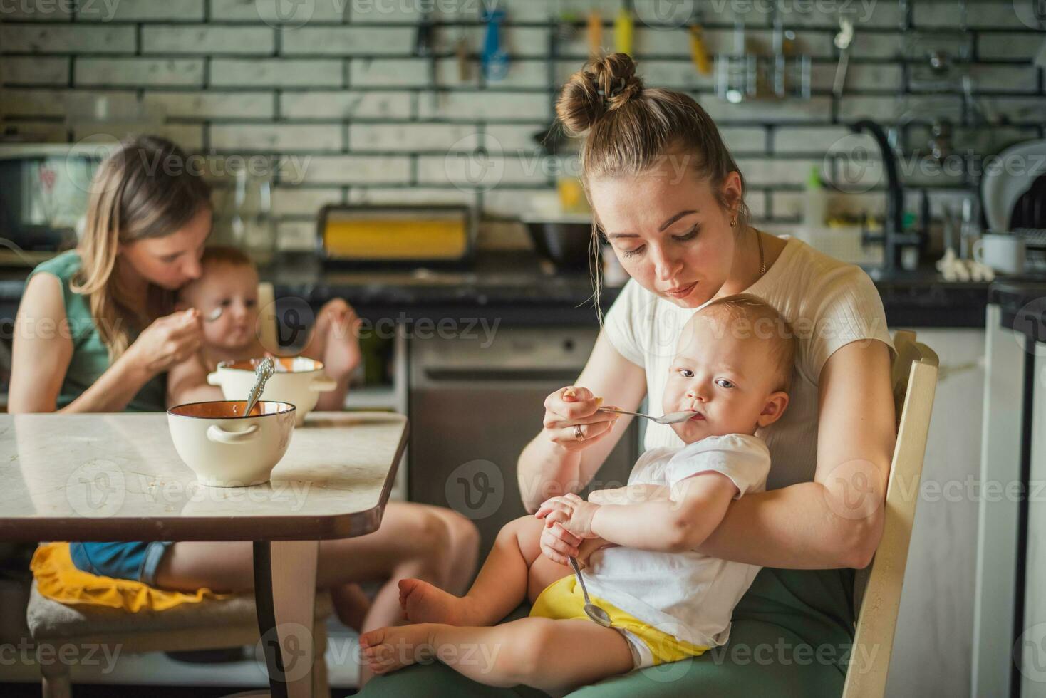 två trött men Lycklig mödrar utfodra deras spädbarn mjölk gröt i de kök foto