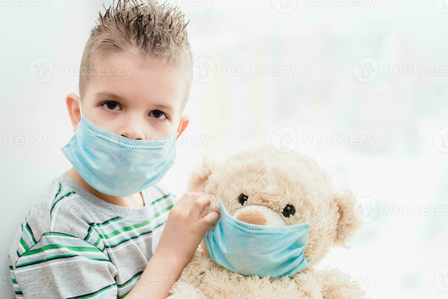 en små barn med en teddy Björn sitter på Hem i karantän i medicinsk masker. förebyggande av coronavirus och covid - 19. foto