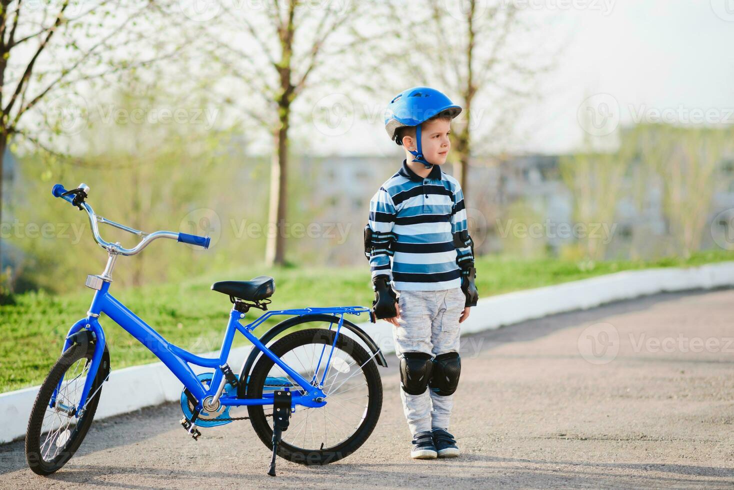 söt barn i hjälm och skydd står nära hans cykel foto