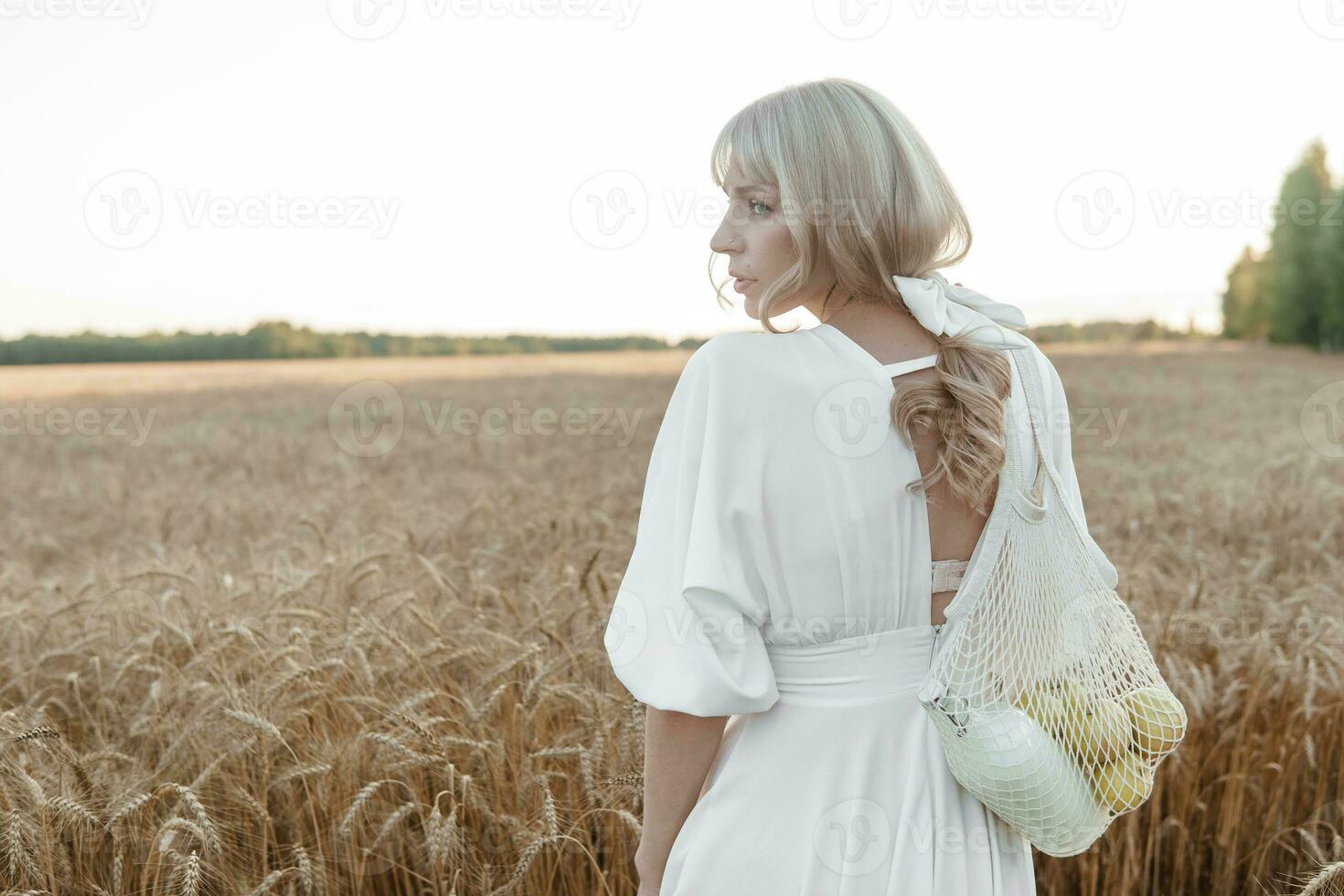 en blond kvinna i en lång vit klänning promenader i en vete fält. de begrepp av en bröllop och gående i natur. foto