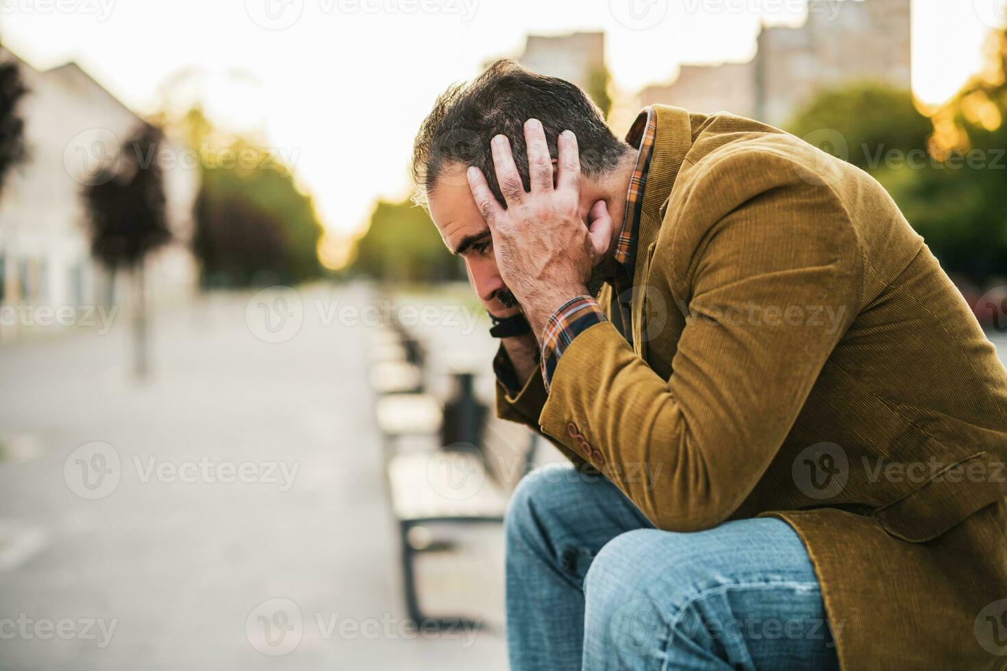 deprimerad affärsman har huvudvärk och Sammanträde på en bänk i de stad gata foto