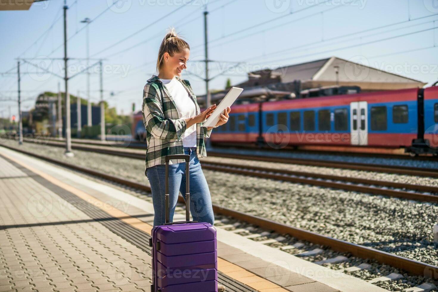 Lycklig kvinna använder sig av digital läsplatta på en tåg station foto