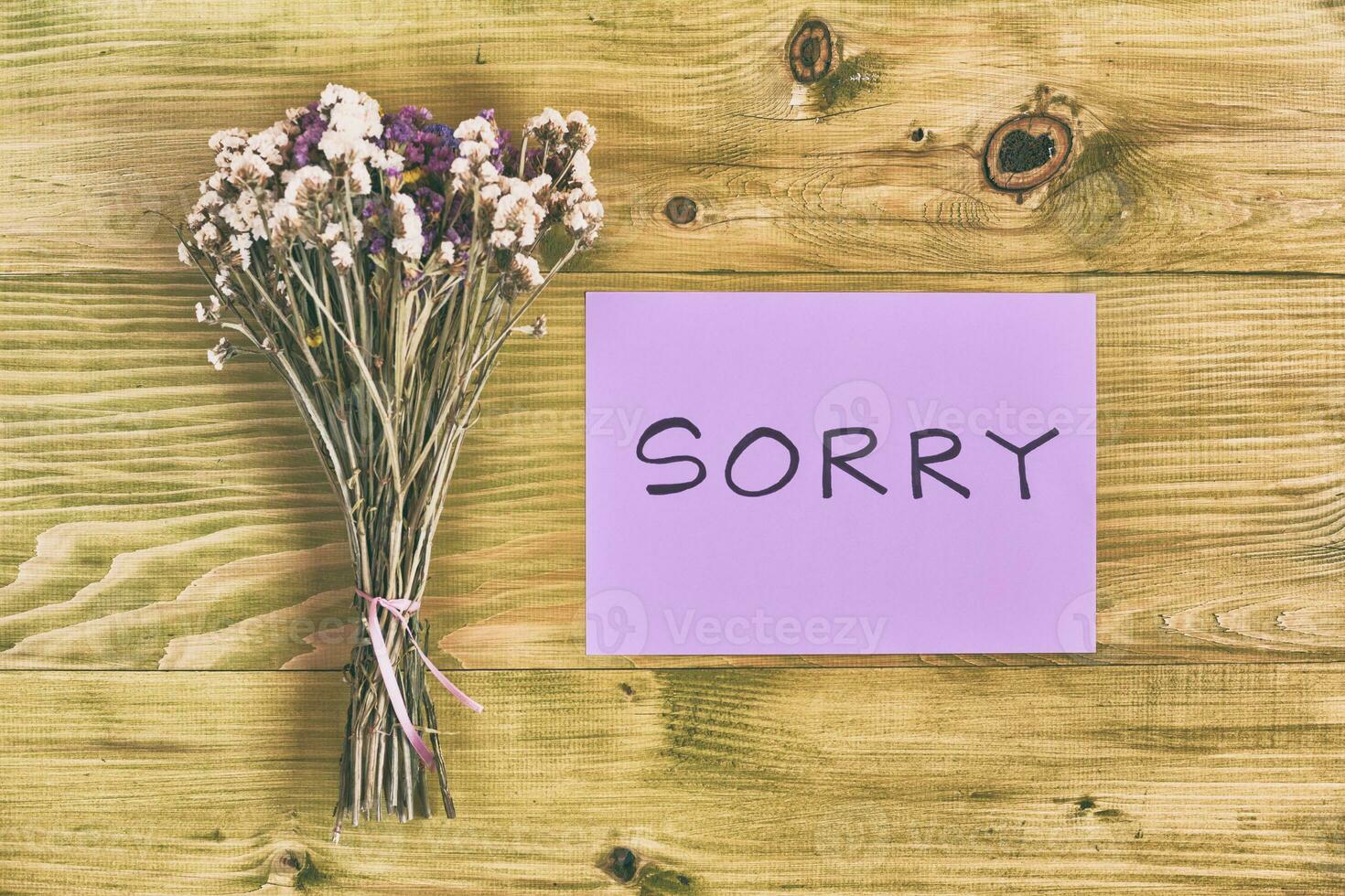 förlåt meddelande på en bit av papper med torkades blommor på en trä- tabell topp se foto