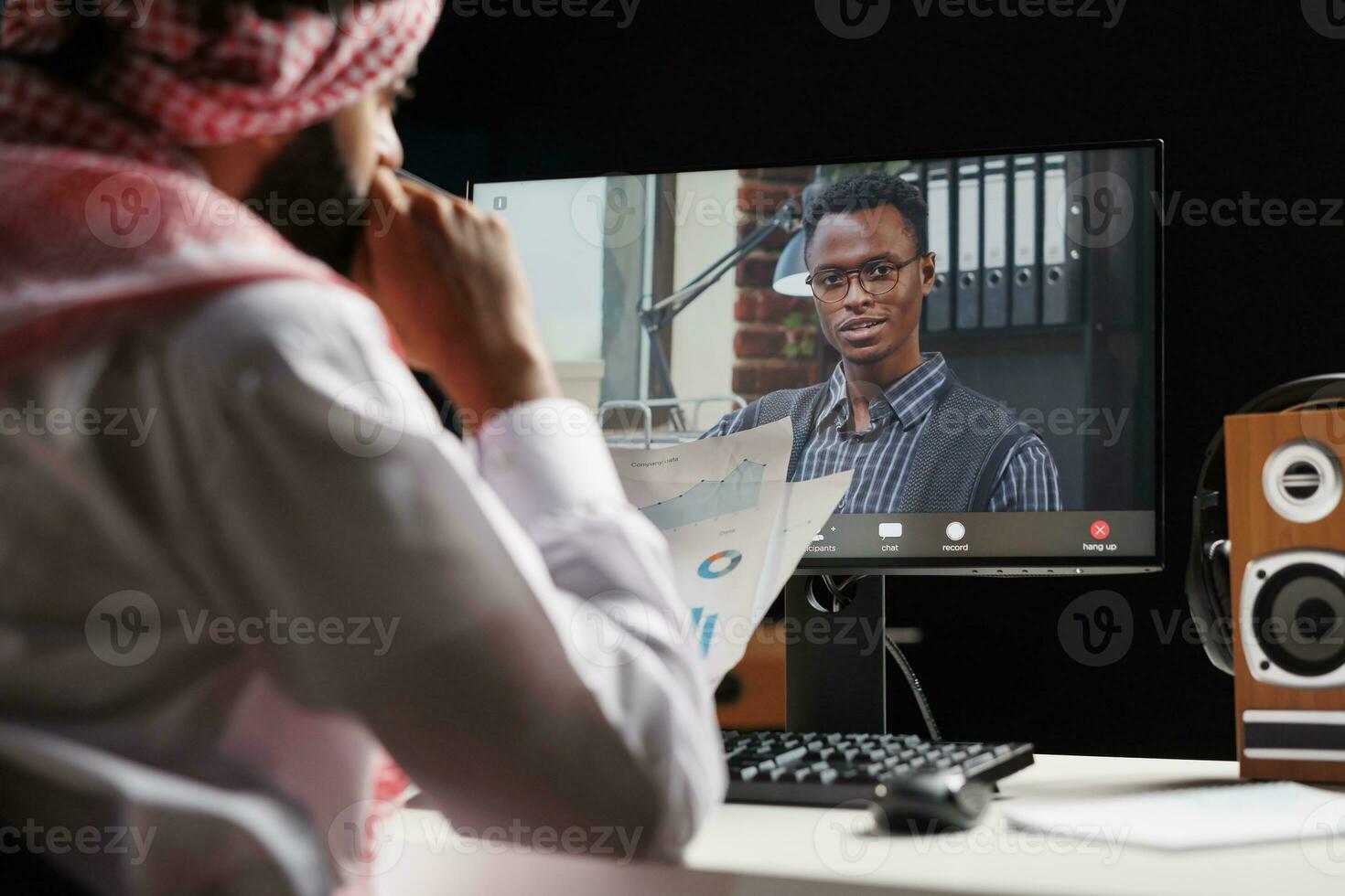 fokusera enbart på dator skärm, de Foto avslöjar en video ring upp happening mellan en muslim affärsman och hans afrikanskamerikansk medarbetare. de bild förmedlar de tekniskt kunniga natur av dessa ung män.