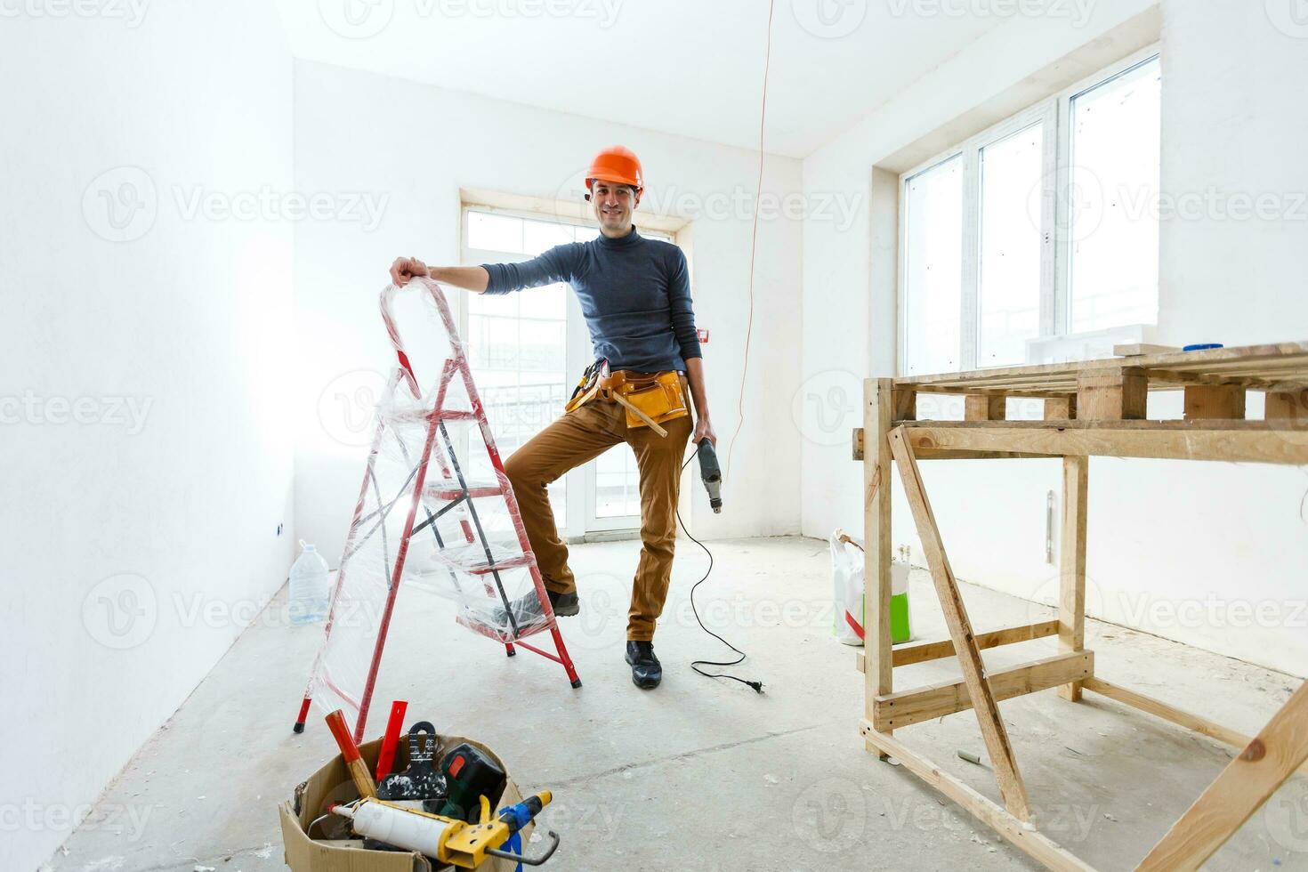 byggaren i en skyddshjälm håller den professionella puncher-hammaren med en borr med stor diameter foto