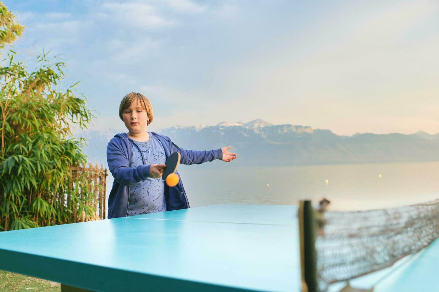 unge pojke spelar ping pong förbi de sjö, aktiva livsstil för barn foto