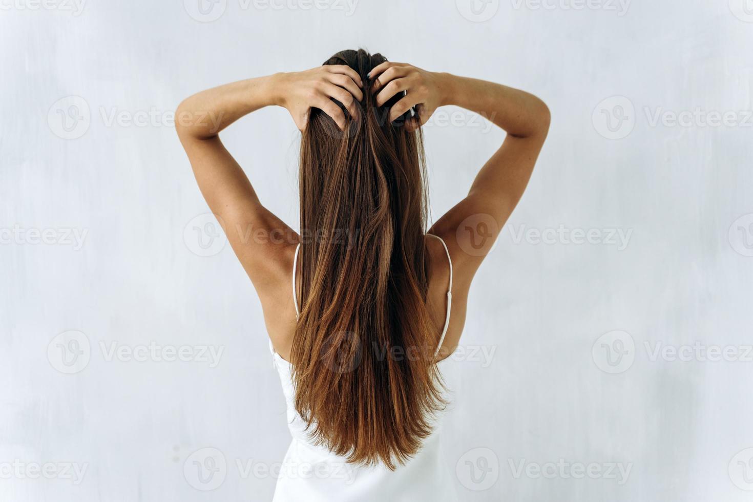 skönhet och vård av hår. midja upp baksidan porträtt av ung brunett dam med räta voluminöst hår vidrör det med händerna. isolerad på vitt foto