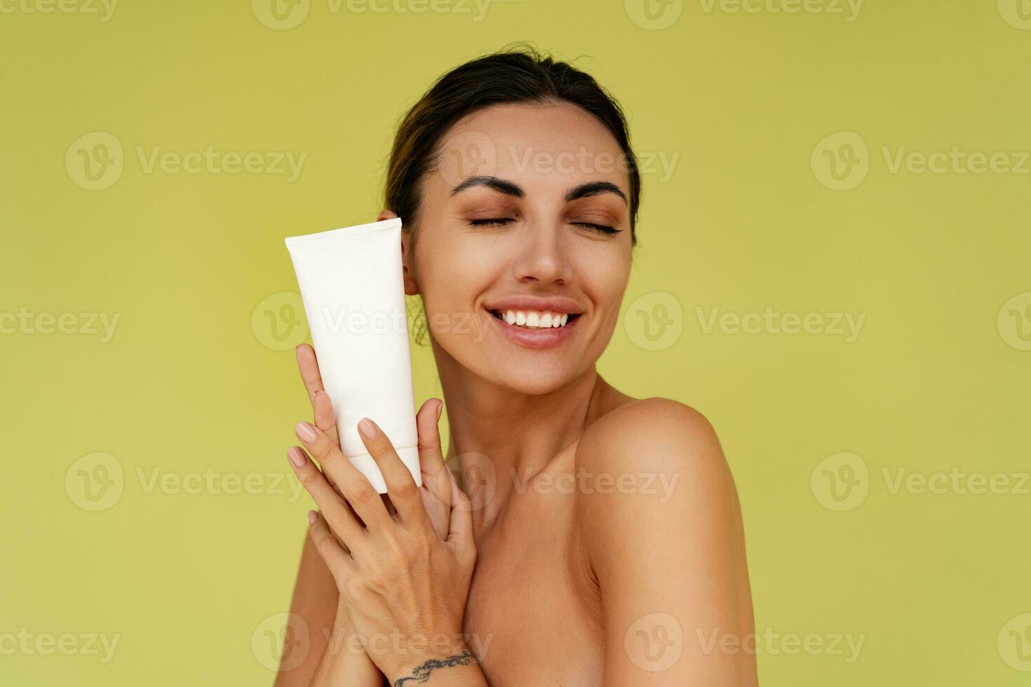 leende kvinna innehar rör med kosmetisk grädde. Foto av attraktiv kvinna med perfekt smink på gul bakgrund. skönhet begrepp