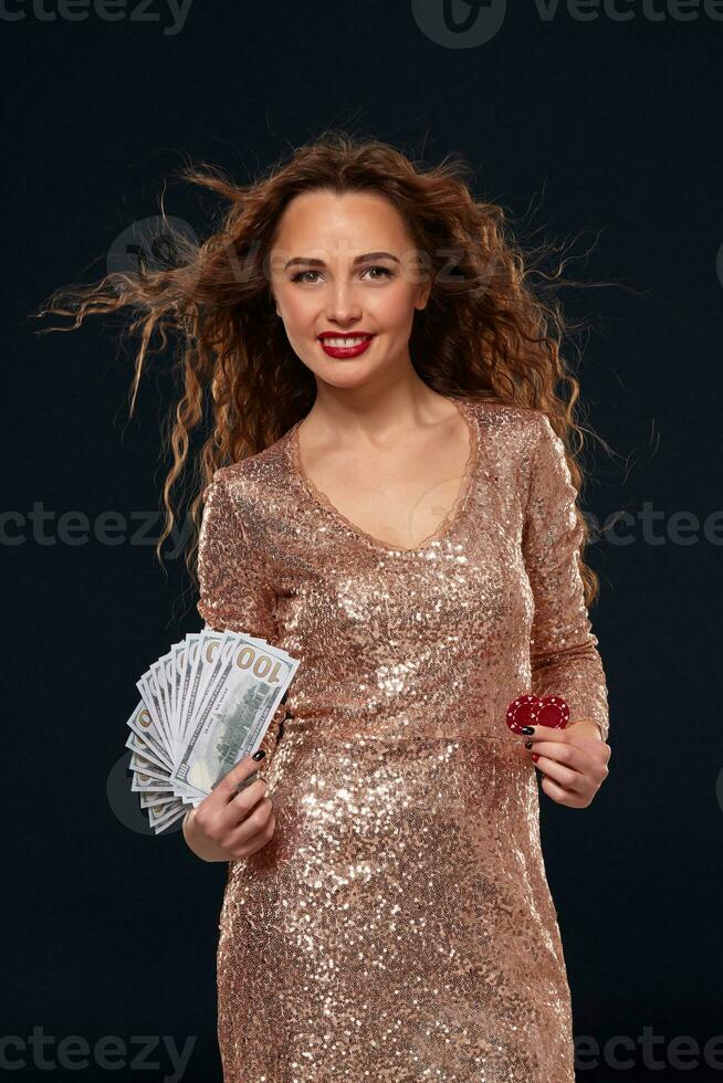 bild av tur- Lycklig kvinna med brun lång hår med fläkt av 100 dollar räkningar, massor av kontanter pengar, över svart bakgrund foto