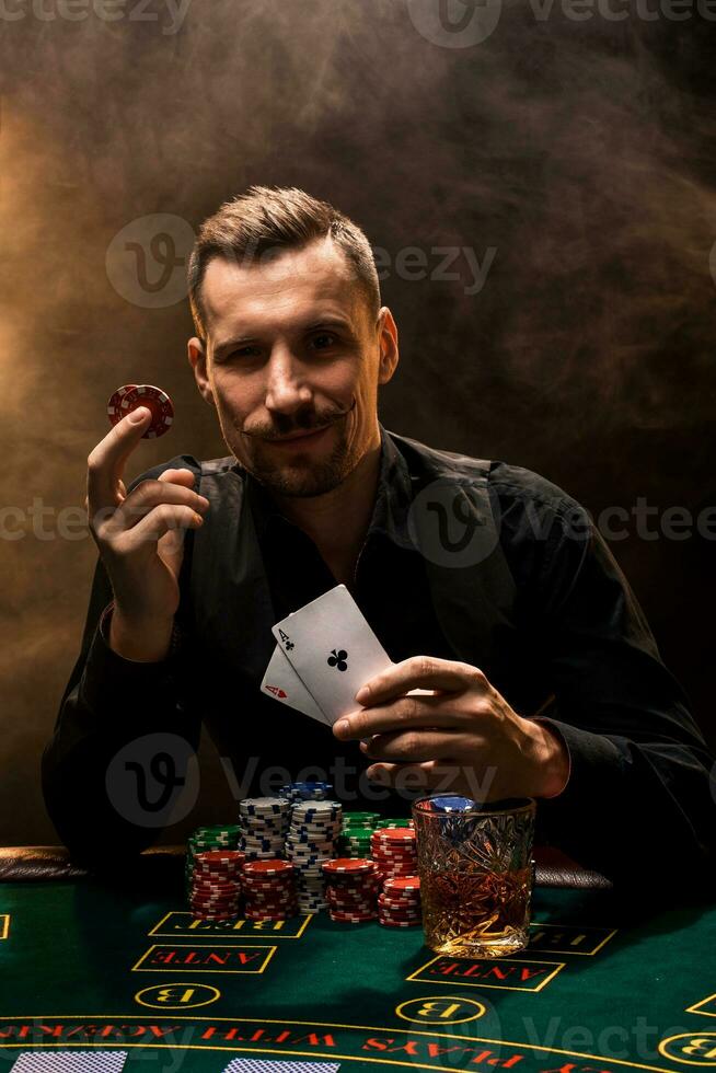man är spelar poker med en cigarr och en whisky, en man visa två kort i de hand, vinnande Allt de pommes frites på de tabell med tjock cigarett rök. foto