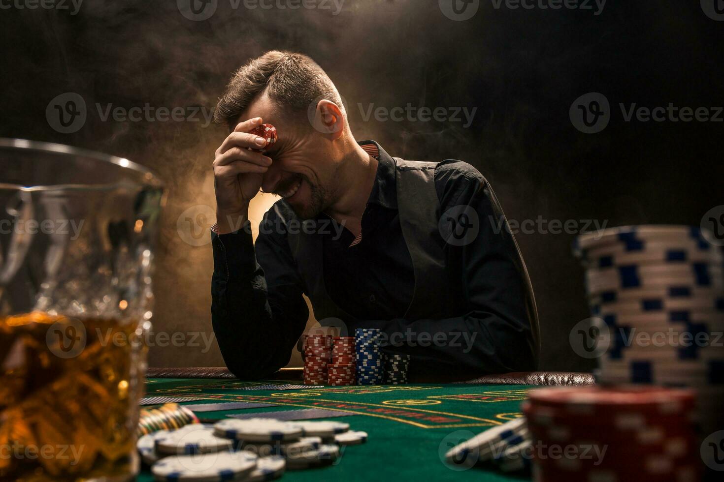 man är spelar poker med en cigarr och en whisky. en man vinnande Allt de pommes frites på de tabell med tjock cigarett rök. foto