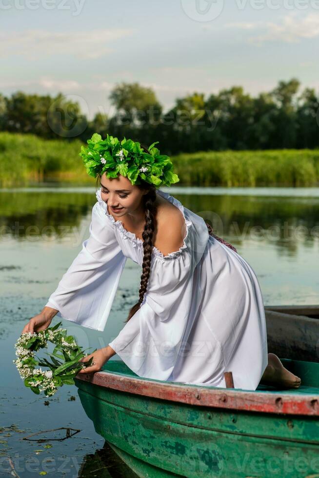 ung sexig kvinna på båt på solnedgång. de flicka har en blomma krans på henne huvud, avkopplande och segling på flod. fantasi konst fotografi. foto