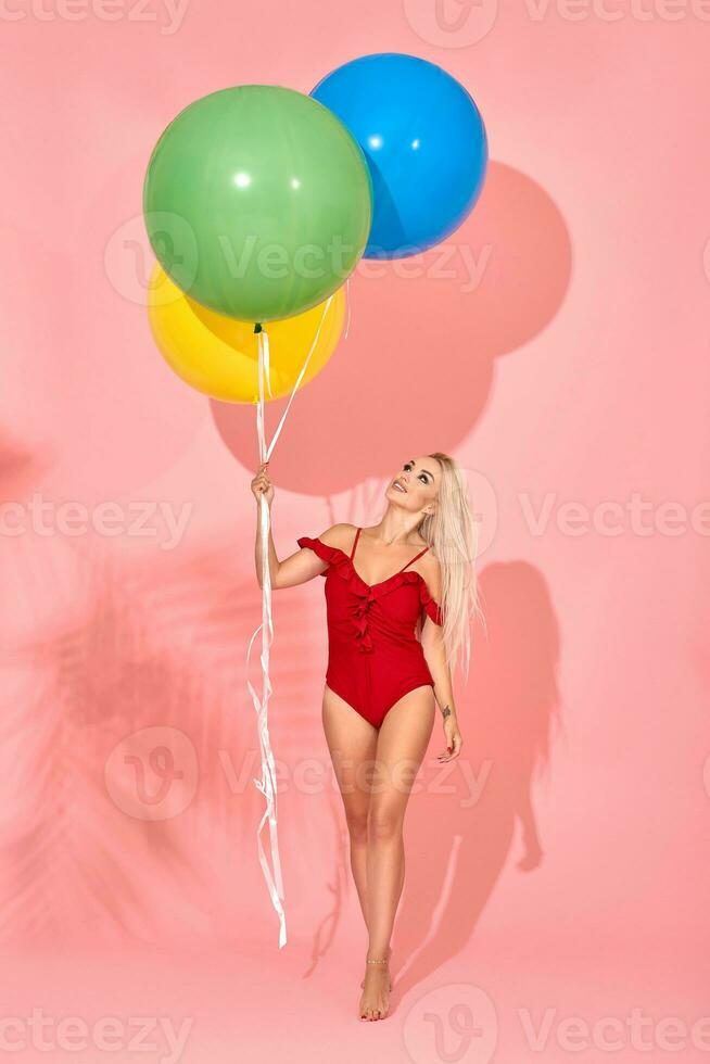 ung sexig smal kvinna i en röd baddräkt med ballonger i henne hand är Framställ i en studio. foto