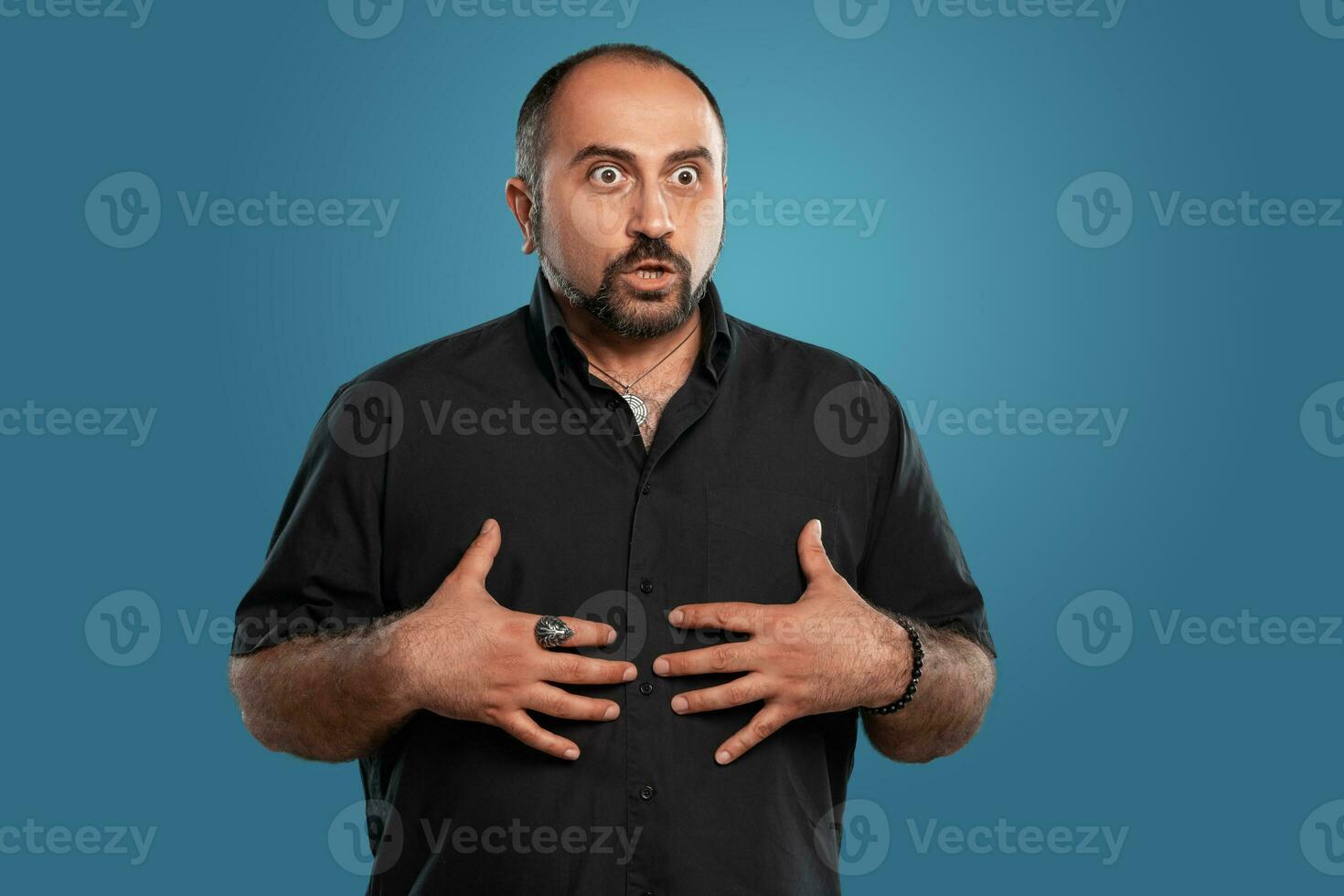 närbild porträtt av en brunett medelålders man med skägg, klädd i en svart t-shirt och Framställ mot en blå bakgrund. foto