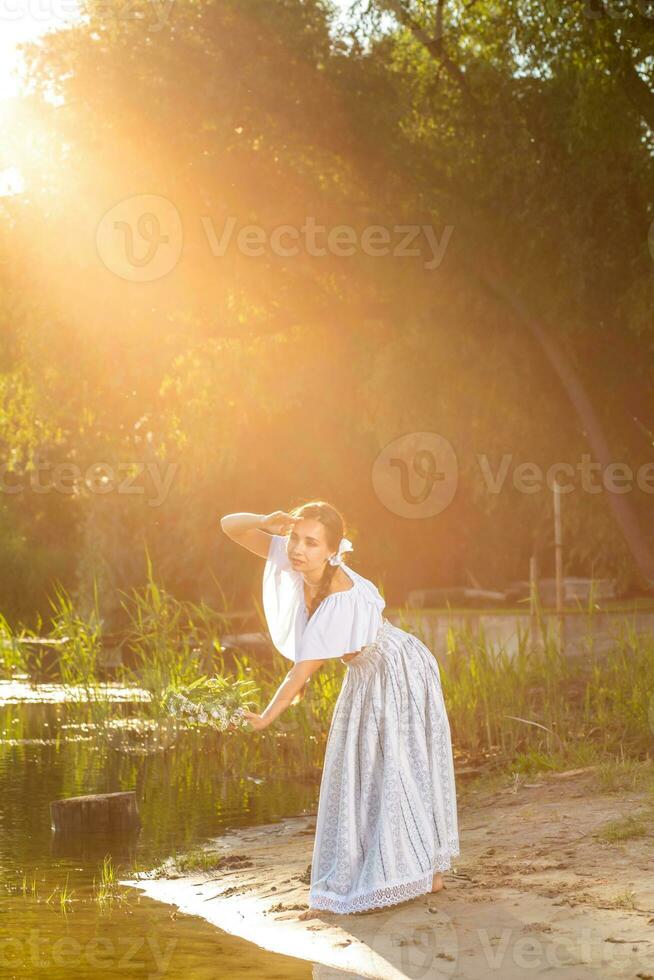 ung skön caucasian kvinna stående på de Bank av flod. traditionell landsbygden bild med flicka på förgrund och kopia Plats. Sol blossa foto