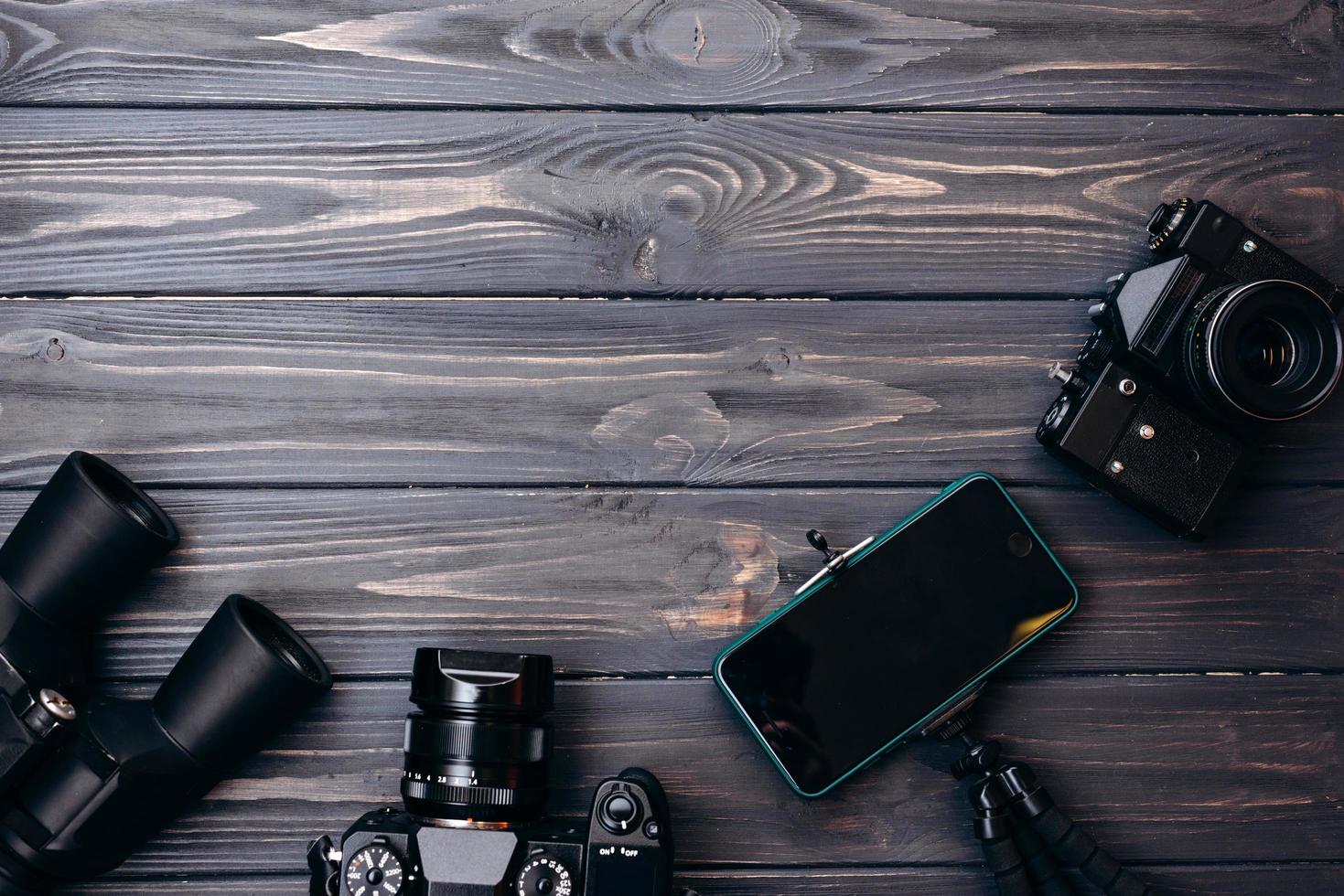 enheter läggs ut på ett träbord kameror, smartphone, kikare. plats för reklam foto